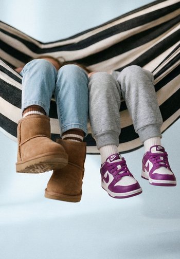 Deux enfants assis dans un hamac rayé noir et blanc, portant des bottes et des baskets, les jambes pendant par-dessus le bord.
