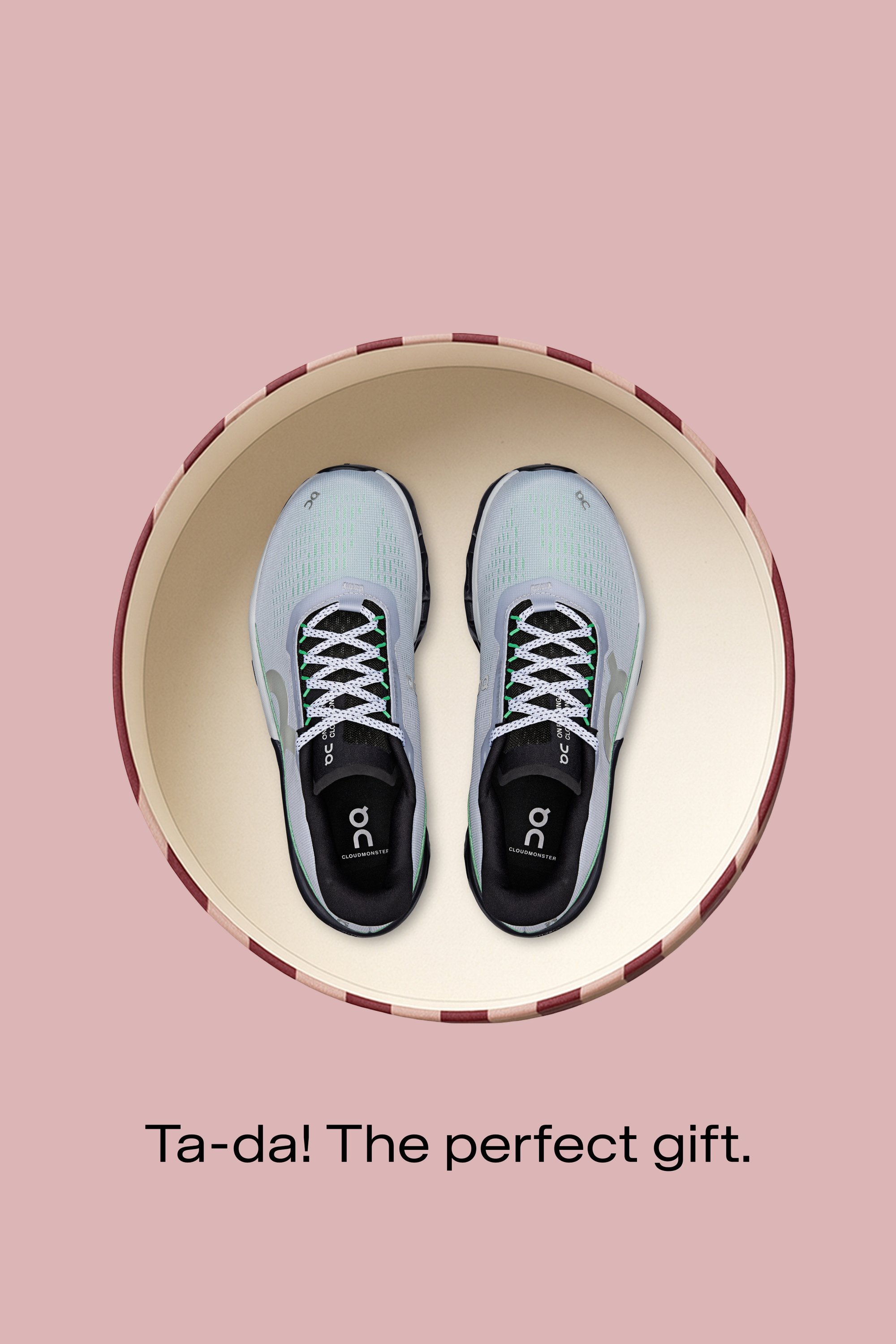 Zapatillas de correr gris claro con suelas negras y detalles en verde. Presentan una parte superior de malla y cordones con patrón, mostradas en una caja redonda beige.