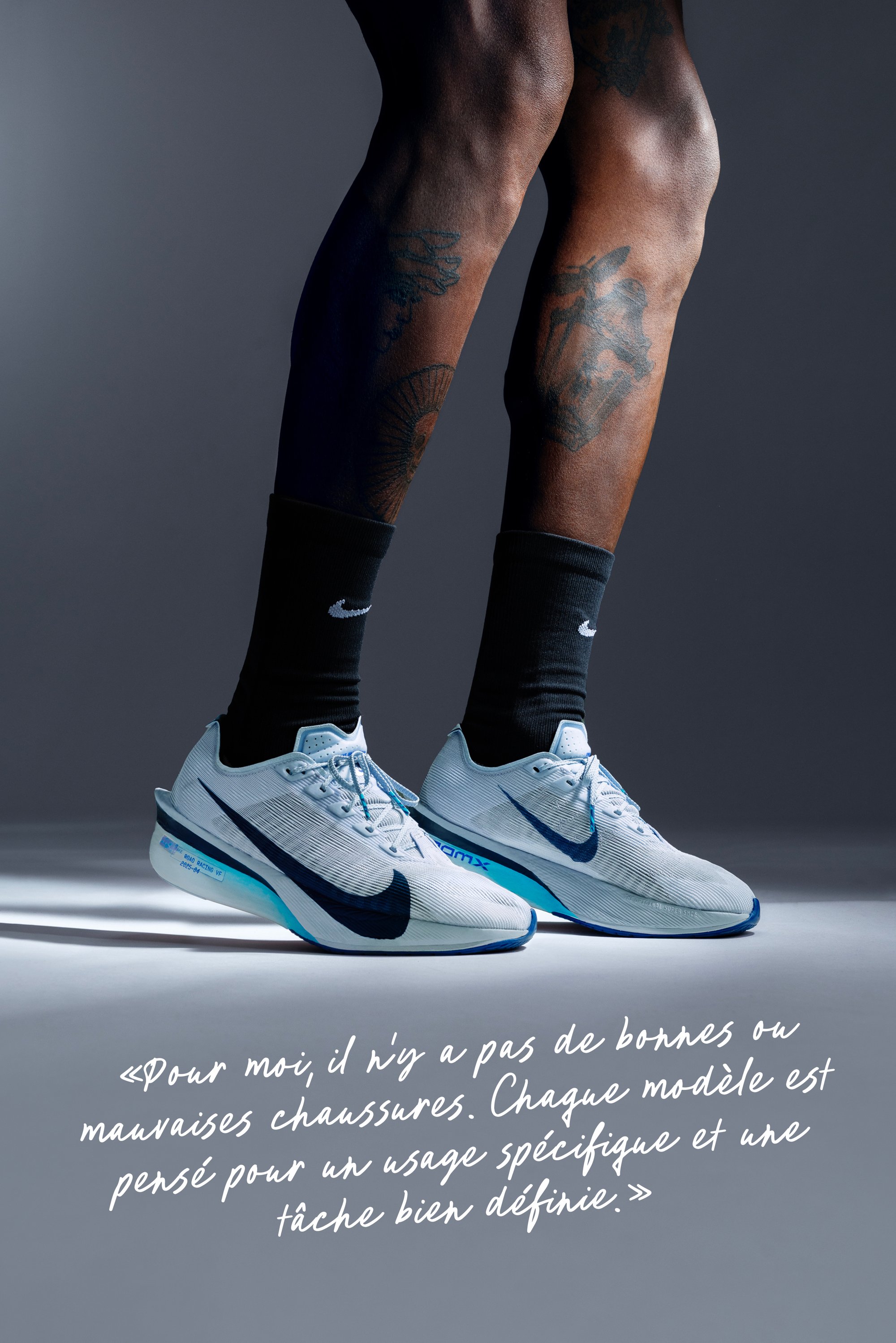 Des chaussures de course Nike bleu clair avec une tige texturée et des accents bleu foncé, assorties à des chaussettes Nike noires, montrant des tatouages complexes sur les jambes.