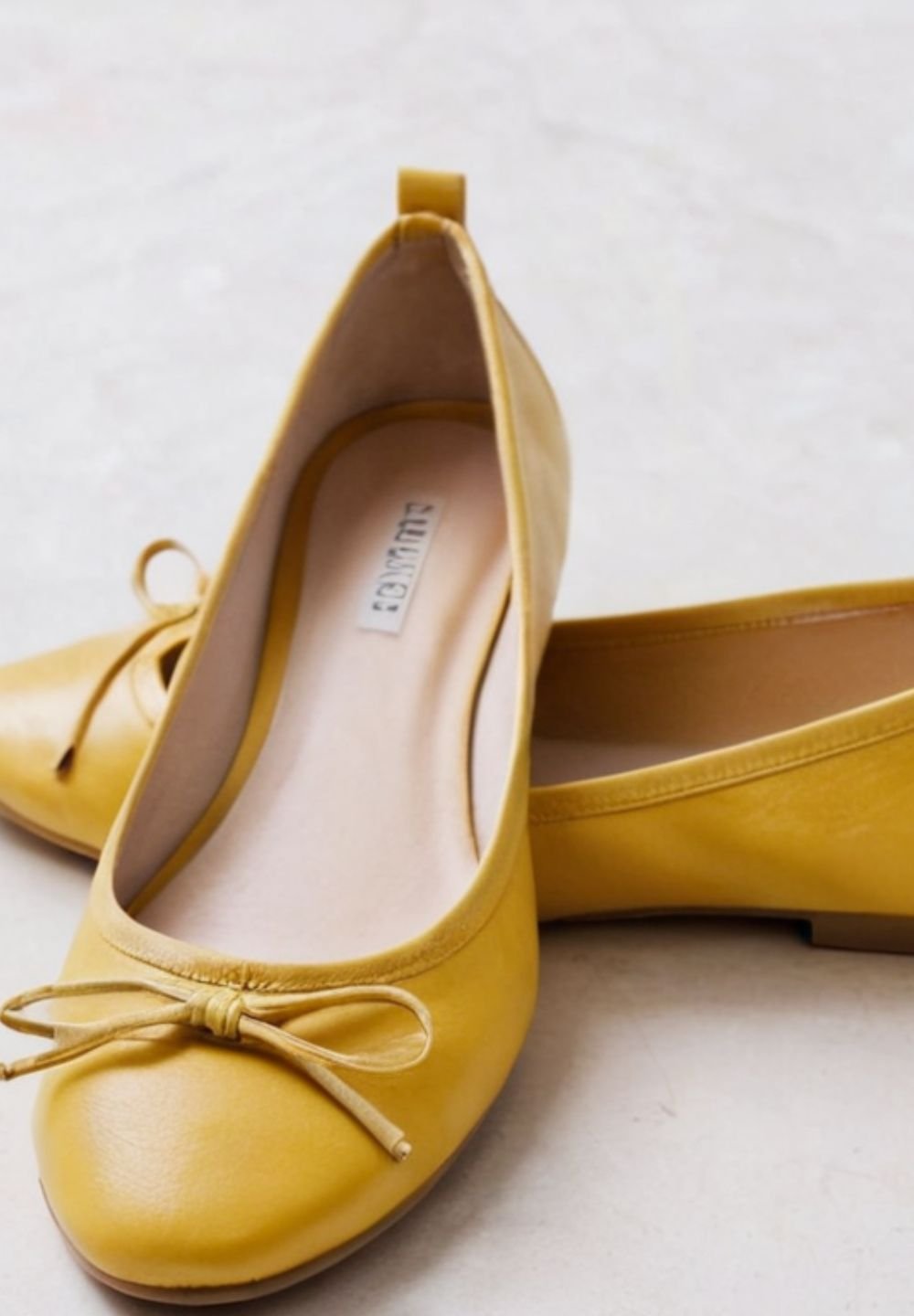 Żółte baletki ze skóry z kokardką, umieszczone na jasnej powierzchni, eksponujące swój gładki wykończenie i zaokrąglone czubki.