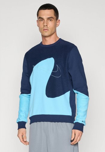 Niebieska i granatowa bluza z dużym, abstrakcyjnym wzorem, teksturowany materiał na ramionach oraz kontrastowe akcenty na rękawach. Logo Nike w zestawie.