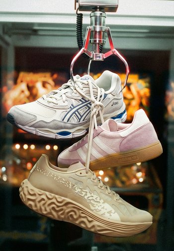Tres zapatos deportivos diferentes colgando por los cordones de la garra de una máquina dentro de un salón recreativo.