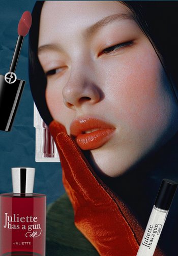 Red lipstick, clear lip gloss, and a crimson perfume bottle in the foreground. A woman with smooth skin and glossy lips is resting her chin on her hand.