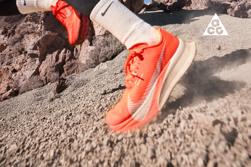 Läufer trägt leuchtend orangefarbene Nike-Schuhe und weiße Socken und sprintet über felsiges, staubiges Gelände in der Nähe von rauen Felsen.