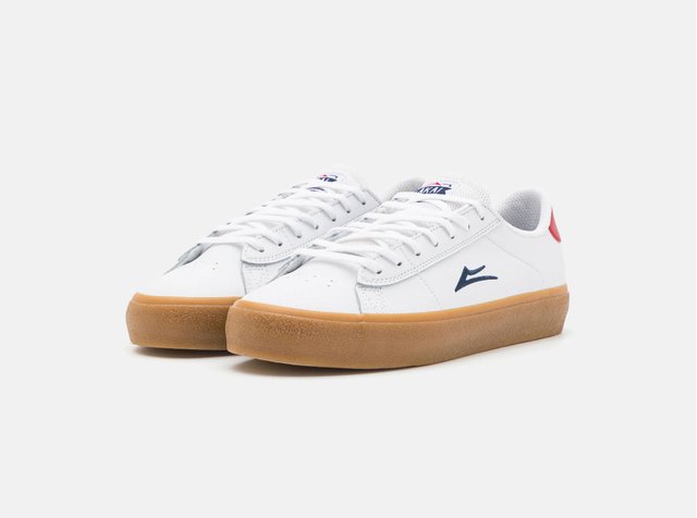 Hvit sneakers med blå og røde detaljer, med en gummisåle, vist i en litt skrå vinkel på en nøytral bakgrunn.