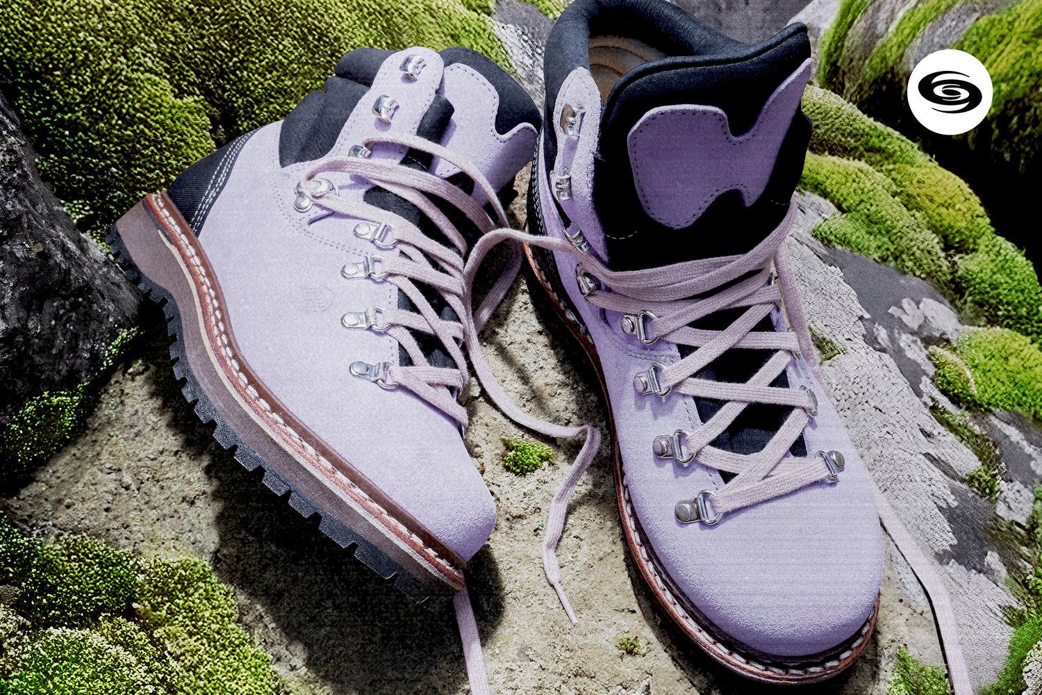Purple hiking boots with black details and laces sit on mossy rocks, highlighting their rugged design and outdoor suitability.