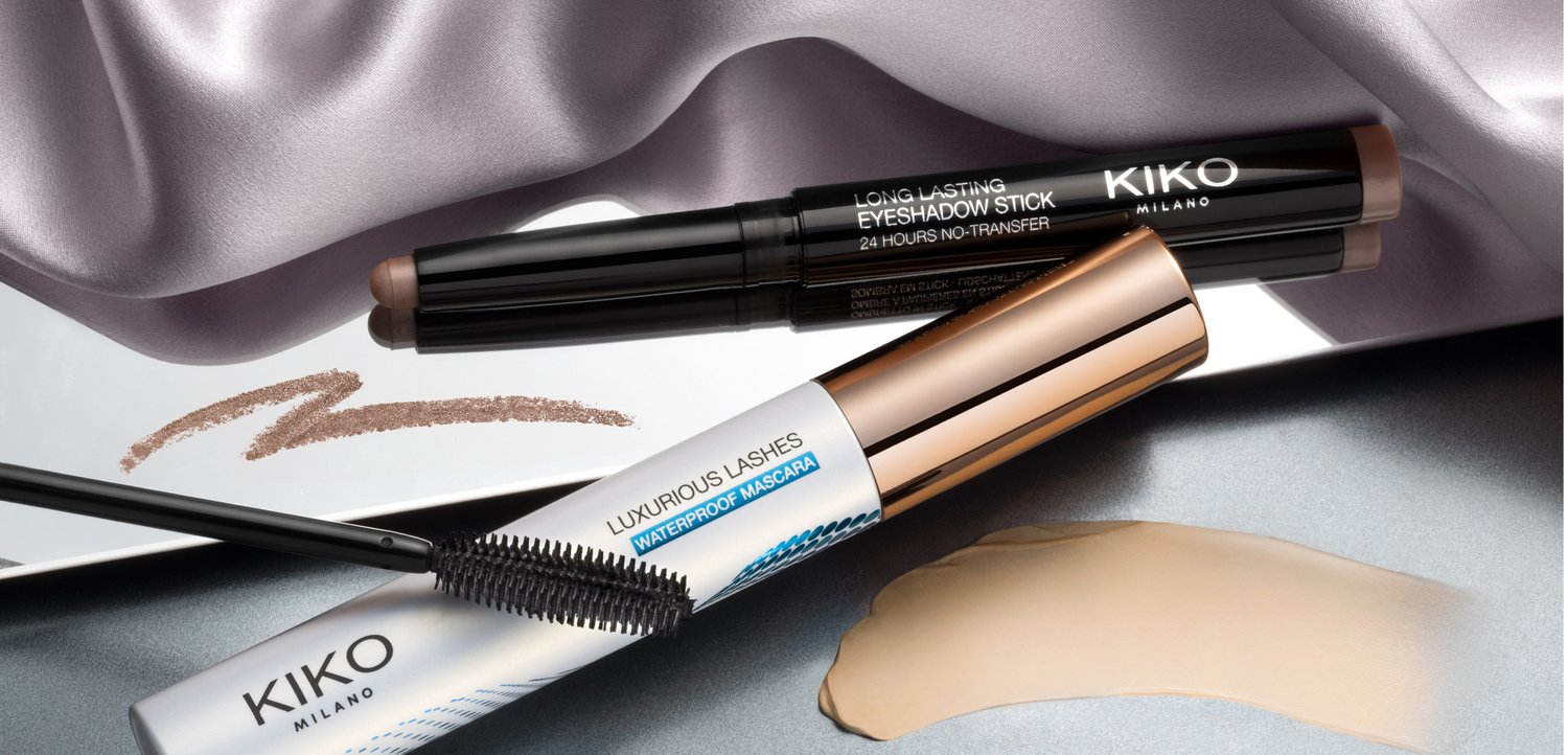 Stick ombretto Kiko Milano e mascara waterproof con campioni di prodotto su uno sfondo di tessuto liscio e lucido.