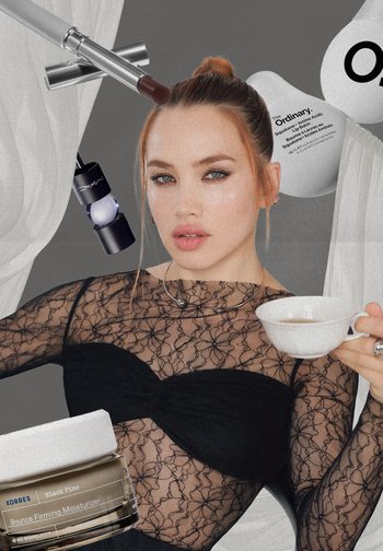 A model in a black lace top holds a white teacup, surrounded by cosmetic products, including a silver lip pencil and jars of moisturizer.