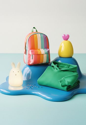 Gefalteter grüner Kapuzenpullover, gestreifter bunter Rucksack, leuchtende Hasenlampe und gelber Gegenstand mit pinkem Herz auf unregelmäßiger blauer Oberfläche.