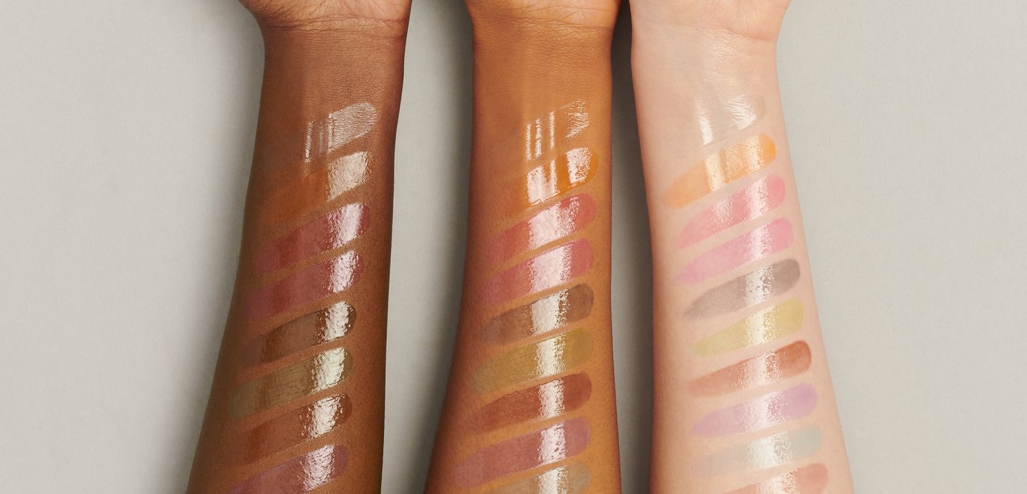 Three arms display glossy lip swatches in varying skin tones. Each arm showcases multiple colors, from deep brown to light peach, with unique finishes.