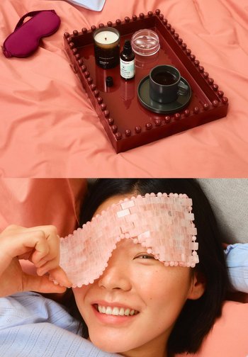 La composición incluye una bandeja de color rojo intenso con detalles redondos, una taza negra, una vela, un suero, un recipiente transparente y una máscara de gel para ojos de color rosa claro.