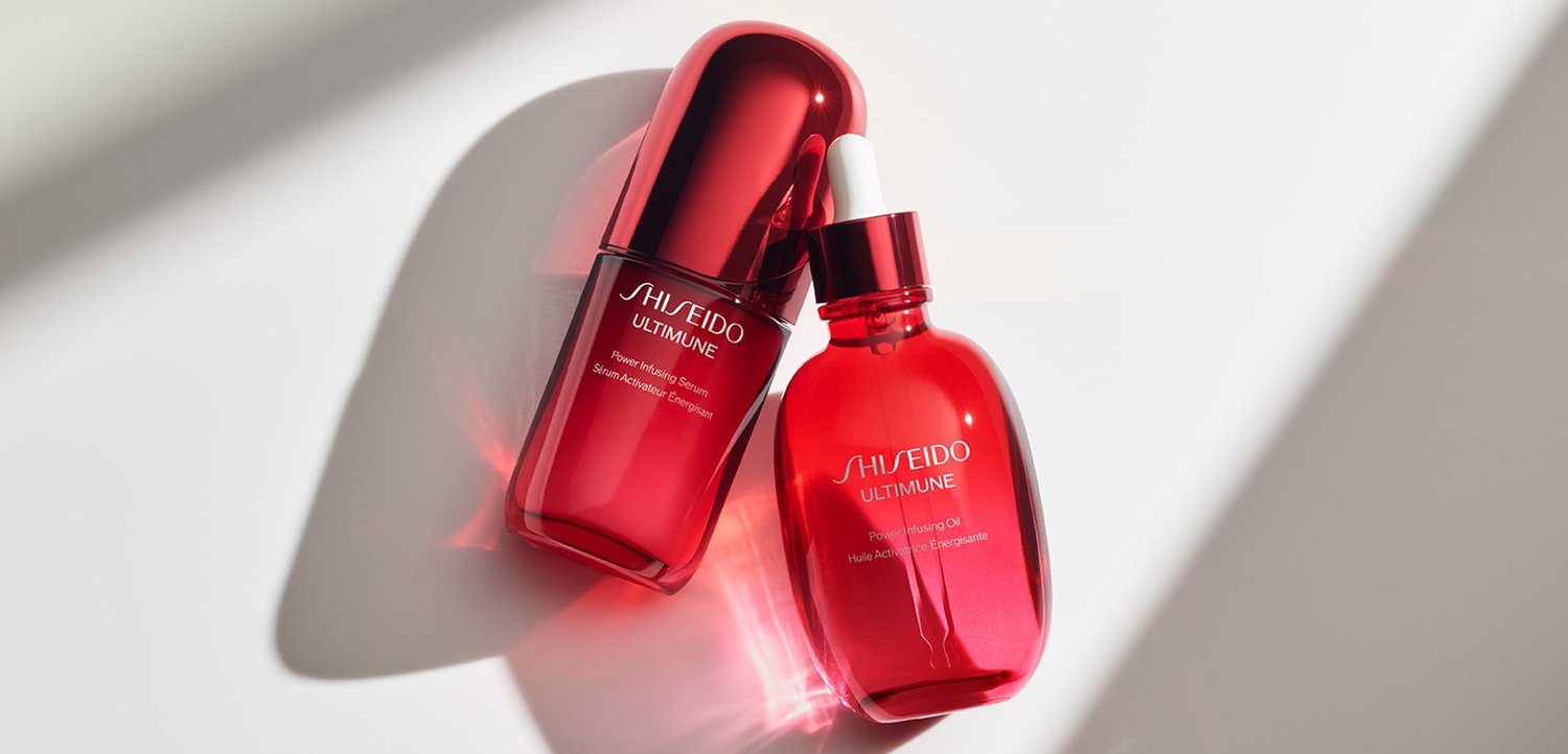 Two red Shiseido Ultimune skincare bottles, one with dropper cap and one capped, casting soft shadows on white surface.
