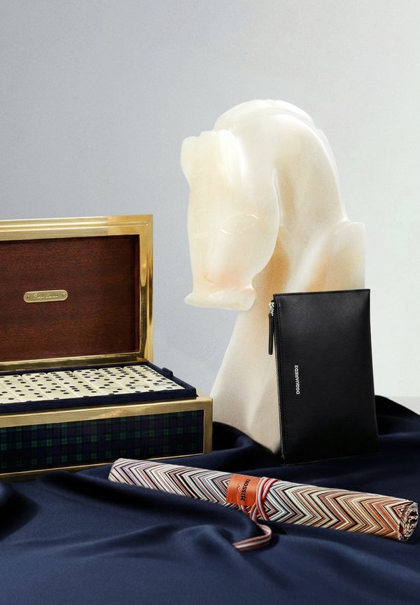 Bolsa de couro preta com fecho, escultura de cavalo branco, caixa de madeira com detalhes dourados, guarda-chuva de tecido com padrão pied-de-poule embrulhado em ziguezague multicolorido.