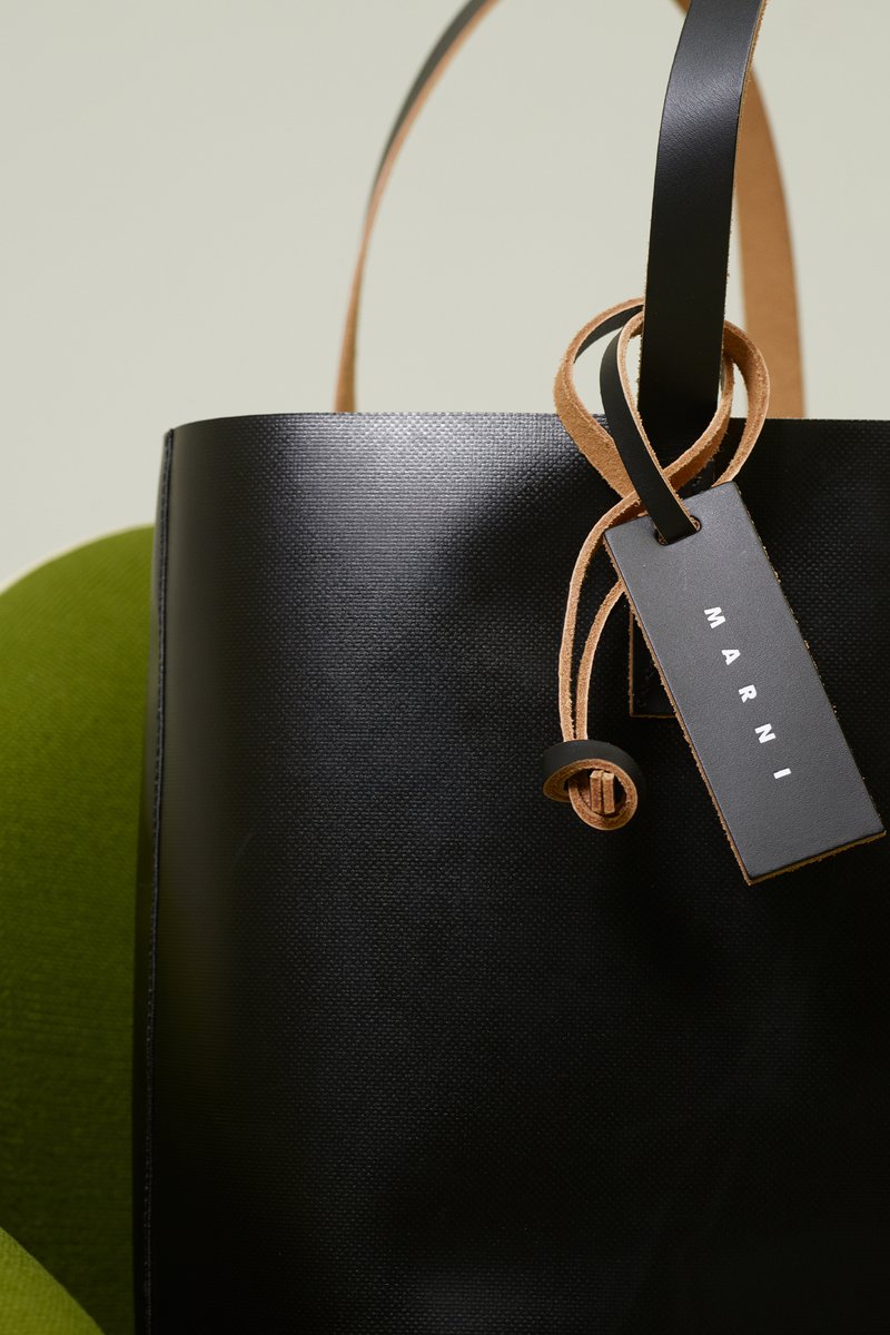 Bolso tote de cuero negro con textura suave. Presenta una correa de cuero marrón claro y una etiqueta con "MARNI" en letras blancas. Los detalles incluyen un nudo decorativo.