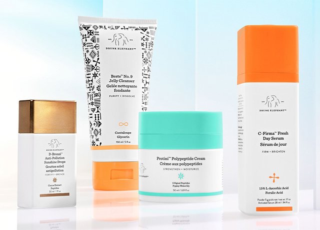 Four skincare products displayed: a white tube with black and white patterns, a teal jar, a white bottle with an orange cap, and a small white bottle with a gold lid.