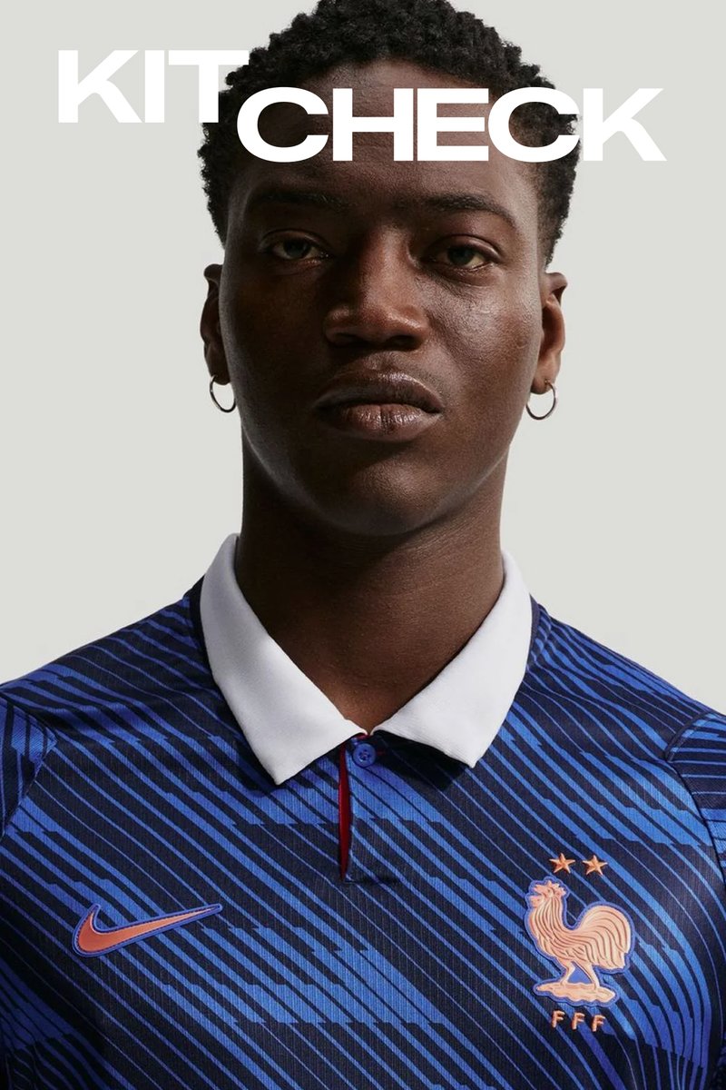 Mann trägt ein blau gestreiftes Frankreich-Fussballtrikot mit weissem Kragen und Nike-Logo, blickt nach vorne vor einfarbigem grauem Hintergrund.