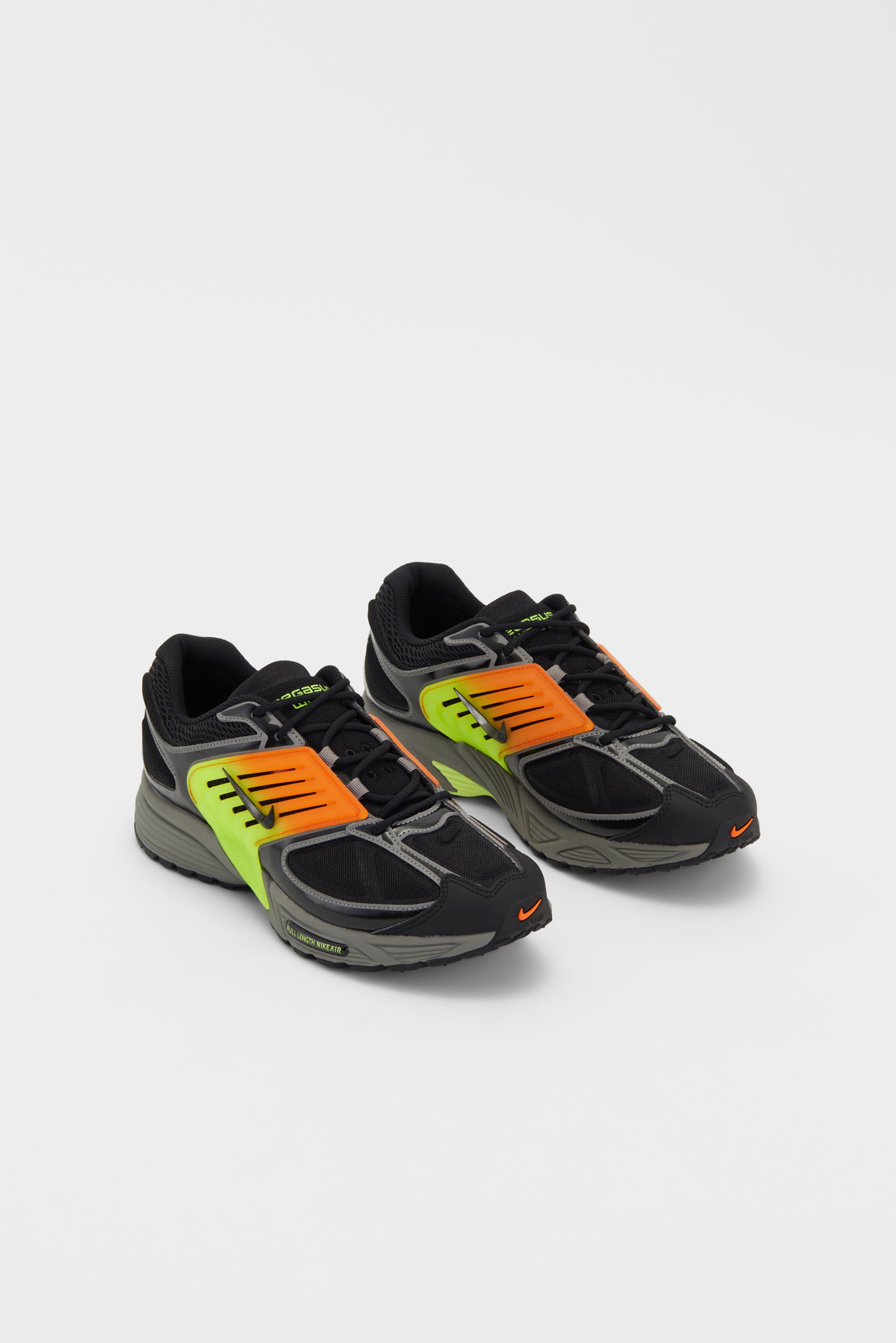 Zwarte en grijze Nike sneakers met felgroene en oranje accenten, geplaatst op een eenvoudige witte achtergrond.