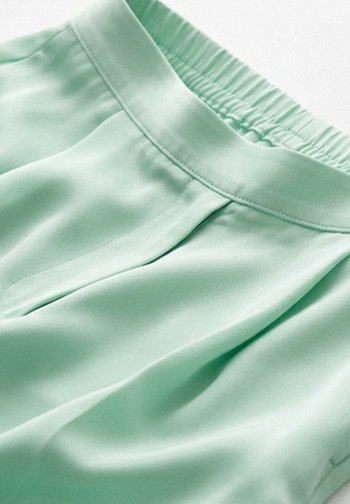 Pantalones de satén verde claro con cintura elástica y detalles de costura que muestran una textura de tela suave y brillante y pliegues suaves.