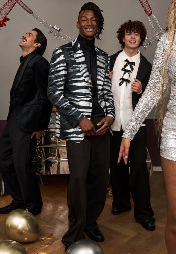 Menn som har på seg forskjellige formelle antrekk: en glitrende striped blazer, en fløyelsdrakt, og en paljettkjole, med ballonger og festlige dekorasjoner i bakgrunnen.