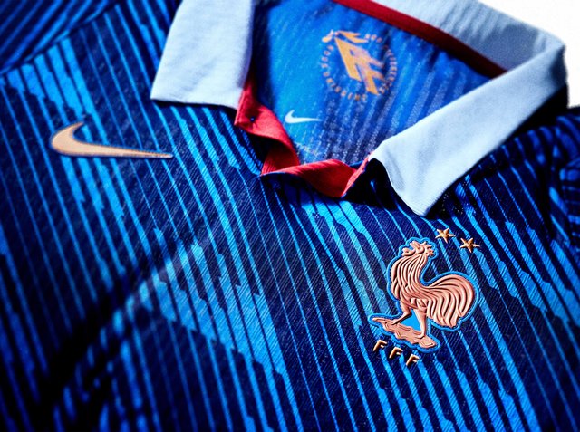 Blaues Frankreichs Fußballtrikot mit rotem Hahn-Wappen, zwei Sternen darüber, weißem Kragen und goldenem Nike-Logo auf gestreiftem Stoff.