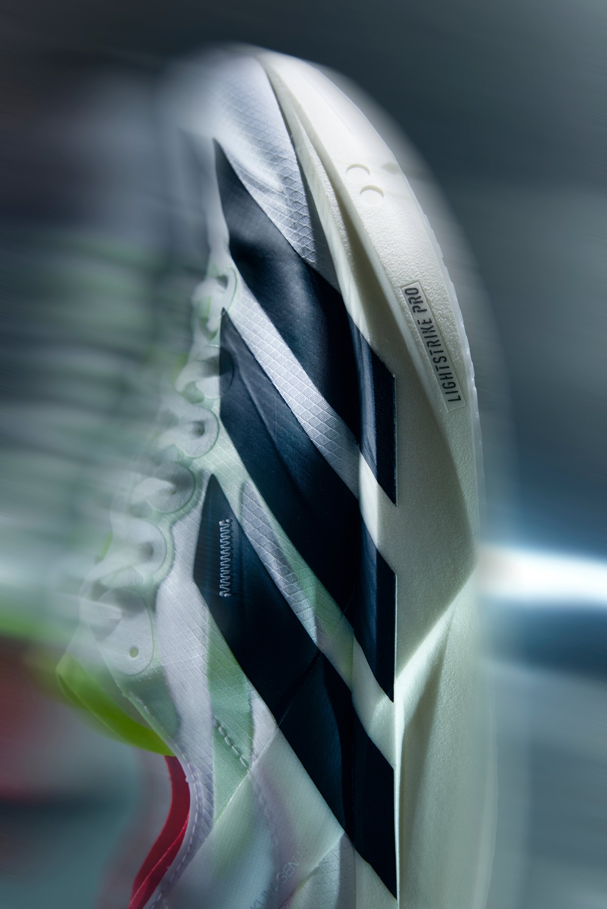 Zbliżenie na białą i czarną biegową butę Adidas z etykietą podeszwy "LIGHTSTRIKE PRO" i widocznymi sznurowadłami.