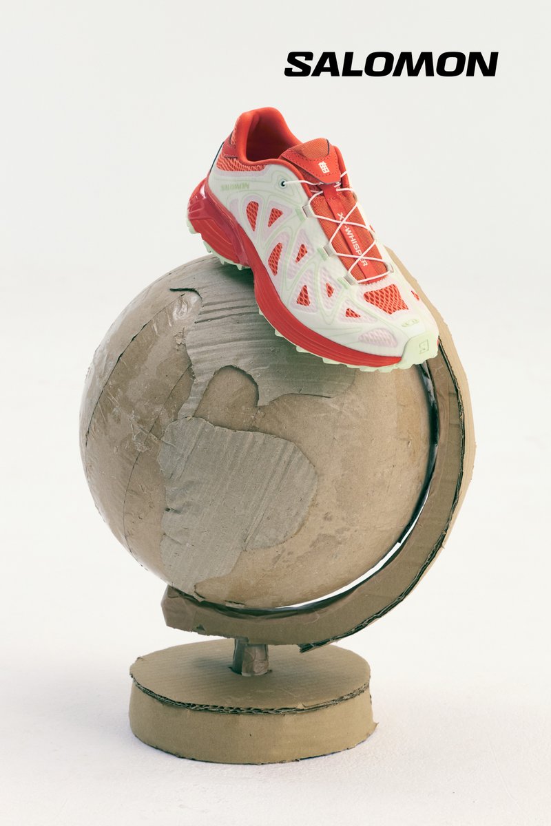 Rote und weiße Salomon-Laufschuhe mit Netzpaneelen, die auf einem Karton-Globusständer sitzen und eine runde Form sowie ein strukturiertes Design zeigen.