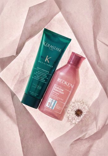 Szampony Kérastase Resistance Bain Thérapiste oraz Redken Volume Injection na różowym, pomarszczonym papierze wraz z główką nasienną dmuchawca.