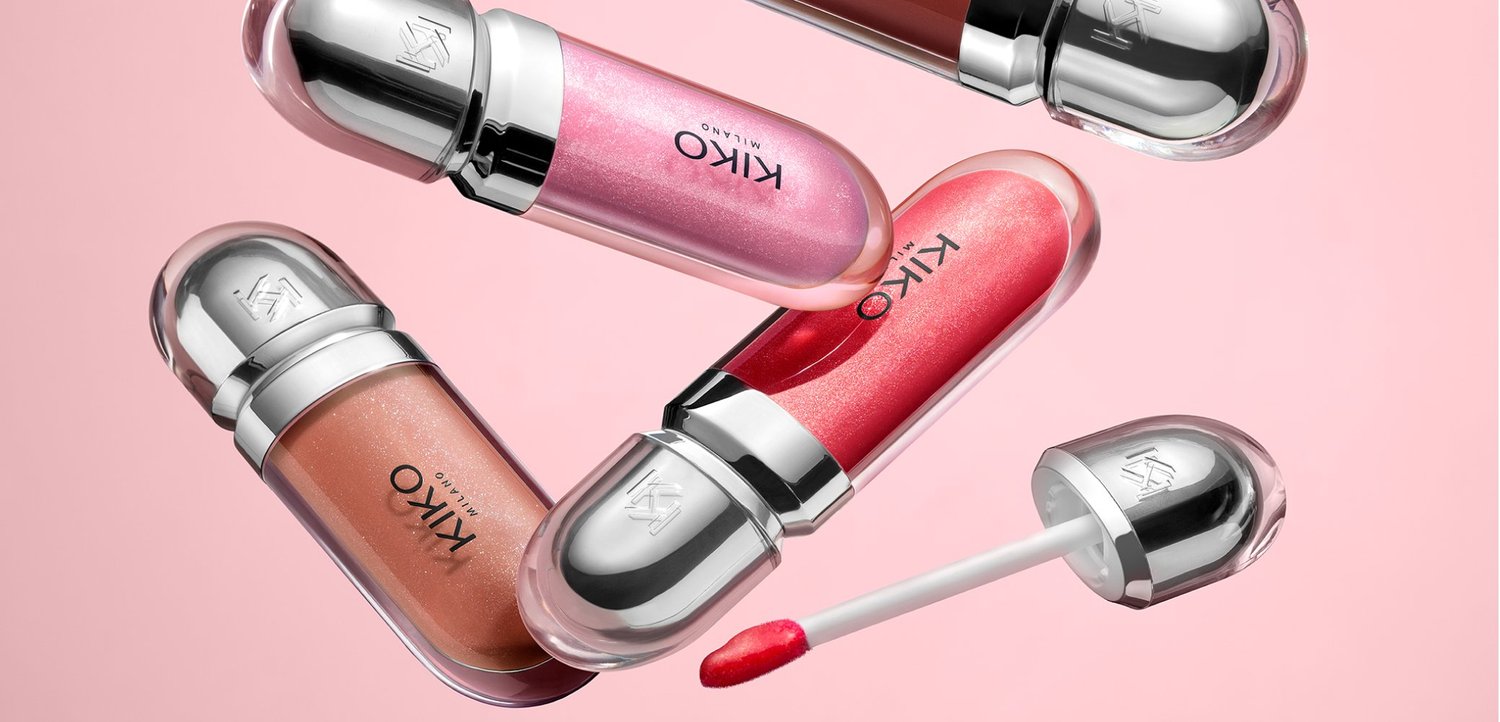 Fünf Lippenpflege-Stifte von KIKO Milano in den Farbtönen Pink, Rot und Nude auf einem rosa Hintergrund, einer offen mit sichtbarem Applikator.