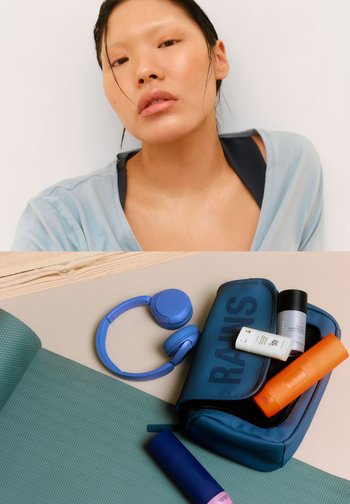 Bolsa impermeable azul con texto "RAINS", que contiene tres productos de cuidado de la piel coloridos. Incluye auriculares azules sobre una alfombra verde texturizada.