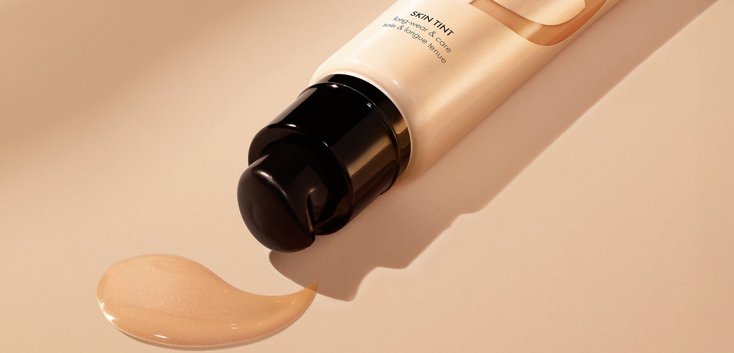 Tube mit getöntem Hautfoundation mit schwarzer Pumpe, die eine glatte, beige Flüssigkeit auf eine passende beige Oberfläche abgibt.