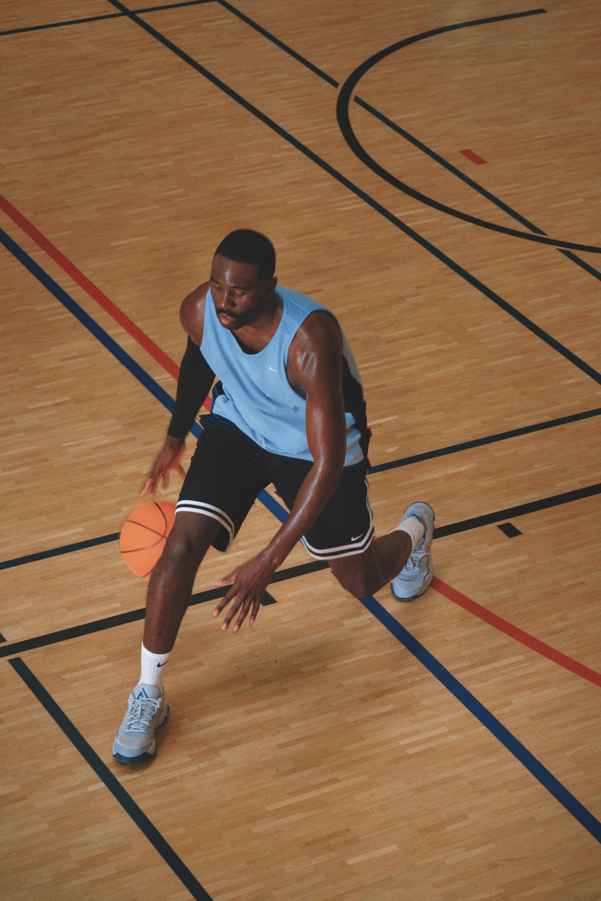 Mannelijke basketballer in een blauwe trui die dribbelt op een binnenbaan met gemarkeerde lijnen tijdens een wedstrijd of training.