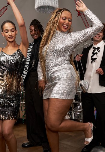 Neljä ihmistä tanssimassa juhlapukeutumisessa; kaksi naista käyttää paljettimekkoja, toinen hopeinen pitkine lettineen, yksi mies mustavalkoisessa puvussa ja solmiolla.