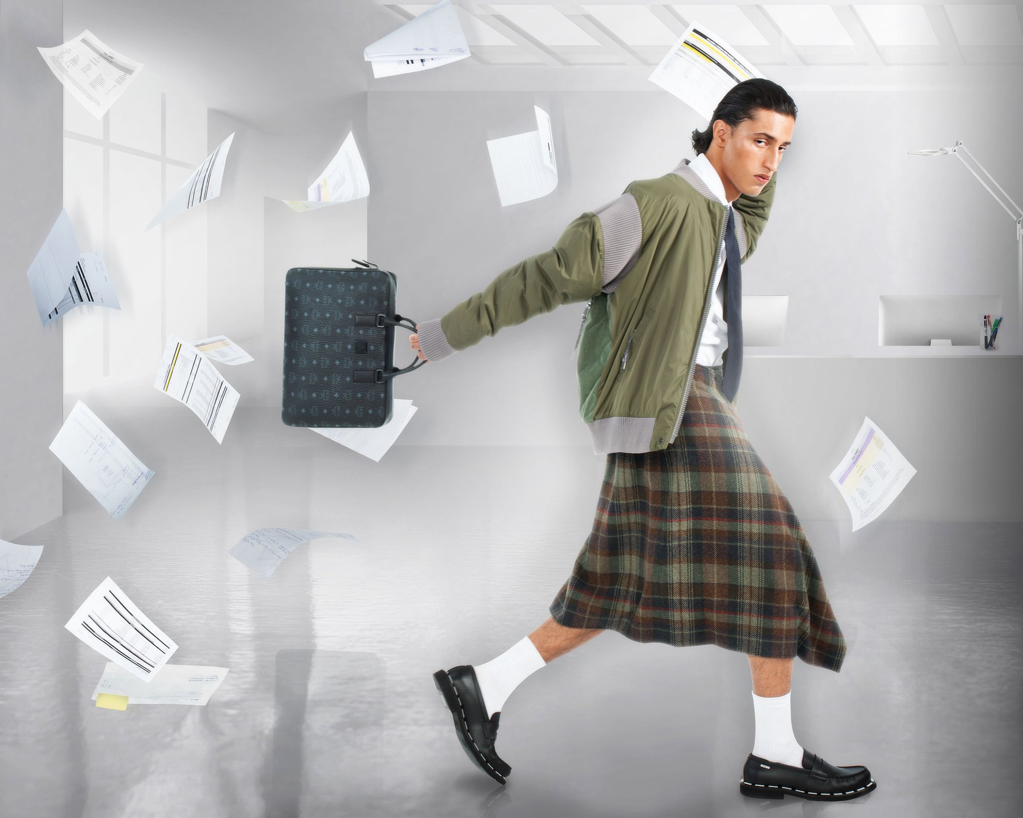 A young man in a plaid skirt and bomber jacket walks briskly, holding a briefcase while documents swirl around him in a modern office space.