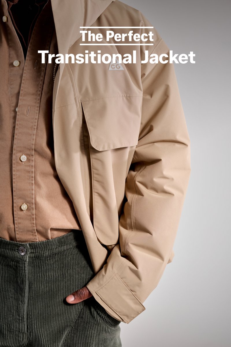 A close-up of a person wearing a beige transitional jacket over a brown shirt, paired with green corduroy trousers and a hand in a pocket.