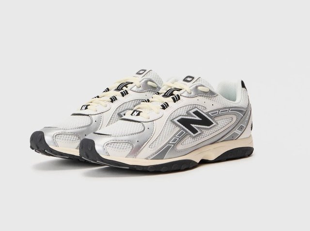 Ασημί και λευκά sneakers New Balance με πλέγμα στην επάνω πλευρά, αντίθετους μαύρους τόνους, παχιά μαύρη σόλα και εξέχουσα λογότυπο στο πλάι.