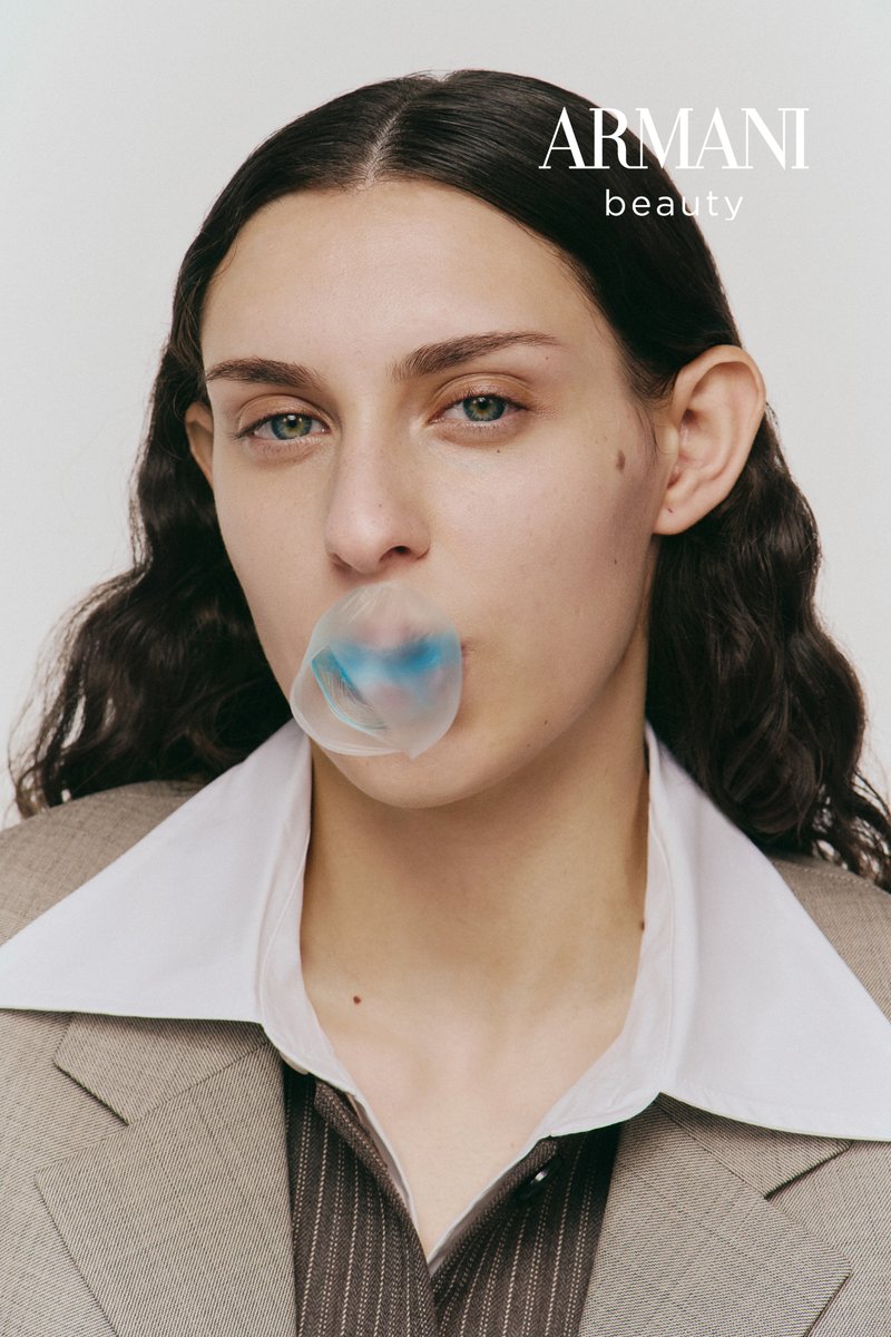 Grijs-witte colblazer met een gladde textuur. Persoon blaast een doorschijnend kauwgombelletje, met een subtiele blauwe tint.