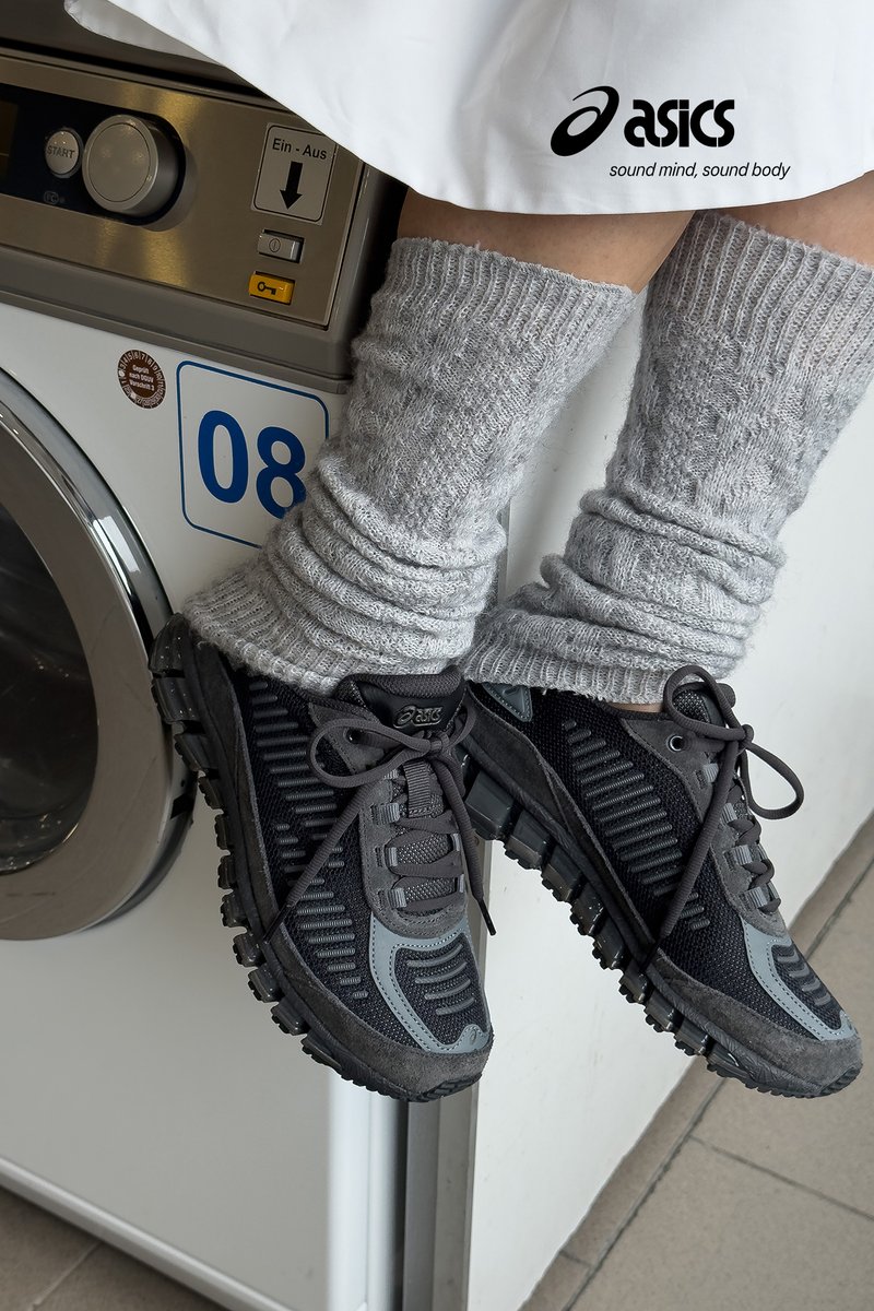 Zwarte en grijze ASICS-schoenen van mesh en rubber, met textuur zijpanelen, veters en een patroon op de zool. Bovenstaande grijze, ribbelige beenwarmers.