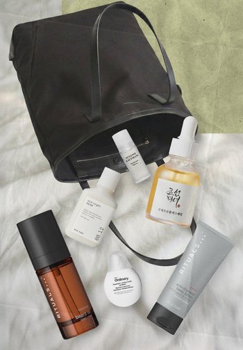 Sac fourre-tout noir sur le lit avec six produits de soins de la peau : huile pour barbe, baume corporel, baume à lèvres, déodorant roll-on, sérum avec compte-gouttes et lotion pour le corps.
