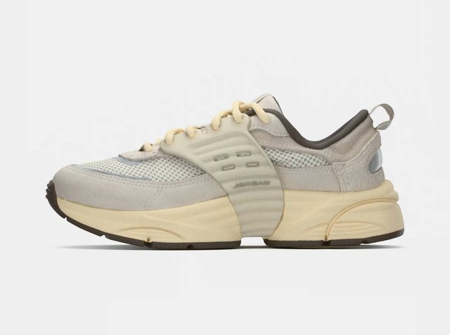 Ανοιχτό γκρι αθλητικό παπούτσι με δικτυωτό επάνω μέρος, λεπτομέρειες από σουέτ και καουτσούκ, στρογγυλεμένη μύτη, χοντρή σόλα και διακριτική σήμανση στο πλάι.