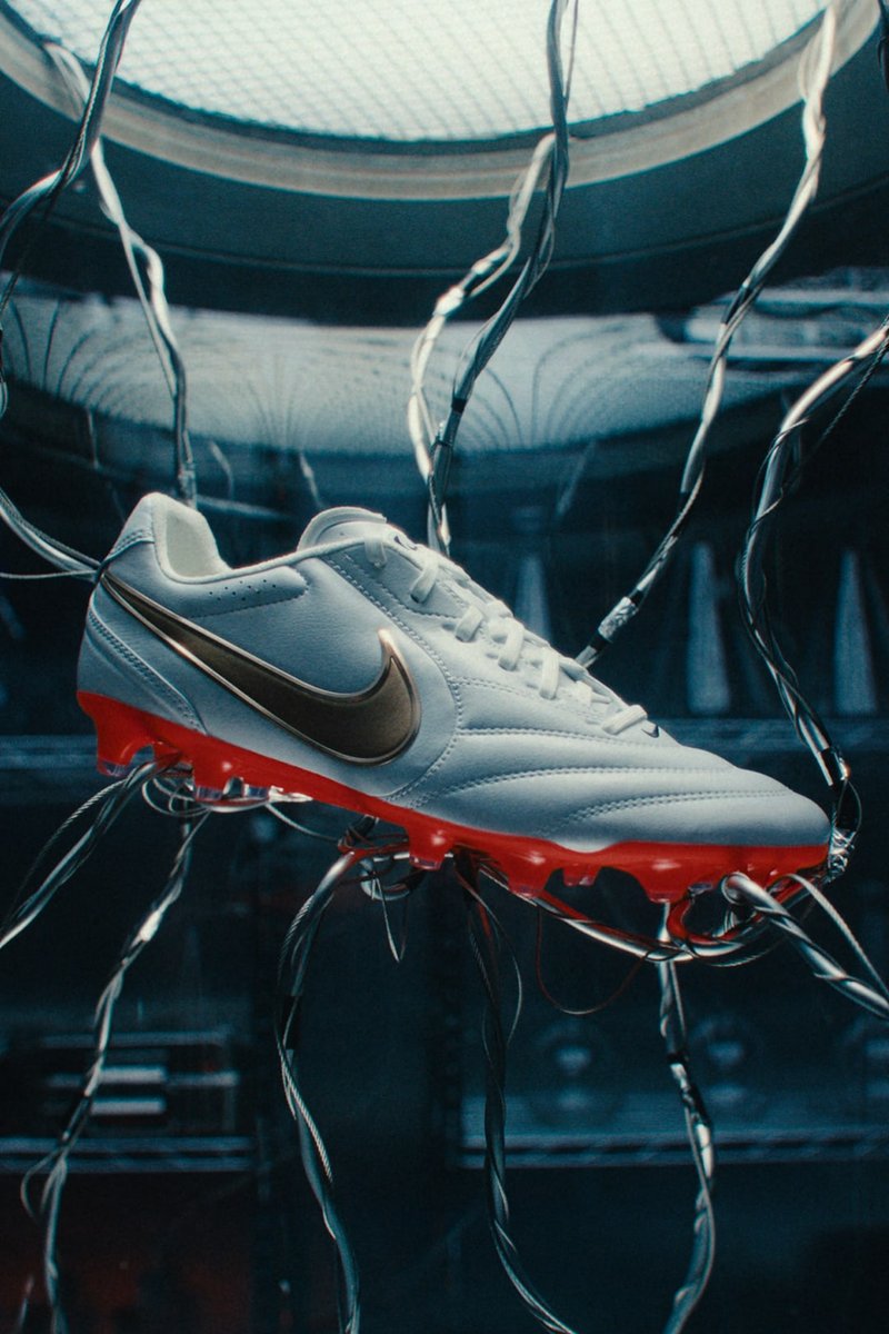 Weißer Nike Fußballschuh mit roter Sohle, an Drähten hängend in einer dunklen futuristischen Umgebung mit einem runden Oberlicht darüber.