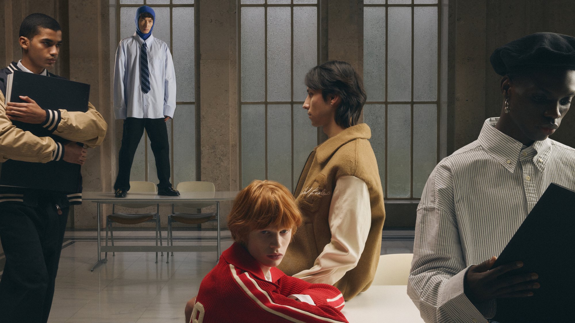 En grupp av fyra personer i avslappnad klädsel, två sitter vid ett bord, en står på det och en håller en mapp, i en modern inredning.