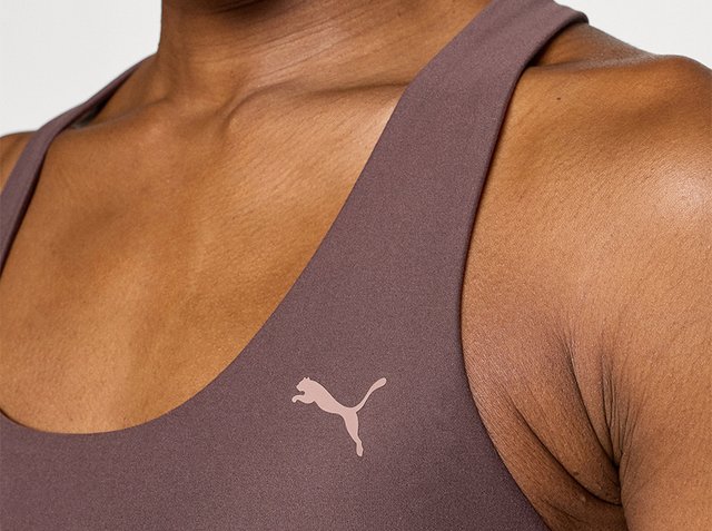 Primo piano di una persona che indossa un reggiseno sportivo marrone con un logo Puma rosa chiaro sulla zona del petto.