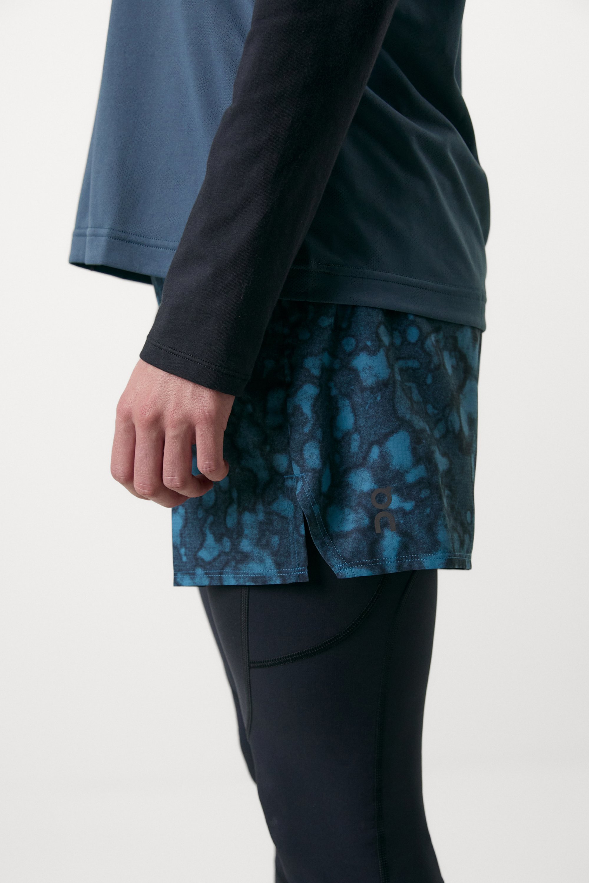 Athlete's side view, wearing a blue short-sleeve top and patterned blue shorts, hand resting on thigh, against a plain background.