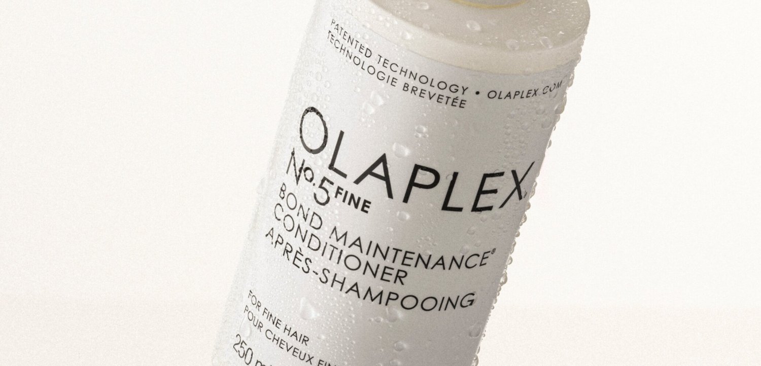 Bottiglia bianca del balsamo Olaplex No. 5 Fine Bond Maintenance con gocce d'acqua sulla superficie, inclinata su uno sfondo chiaro.