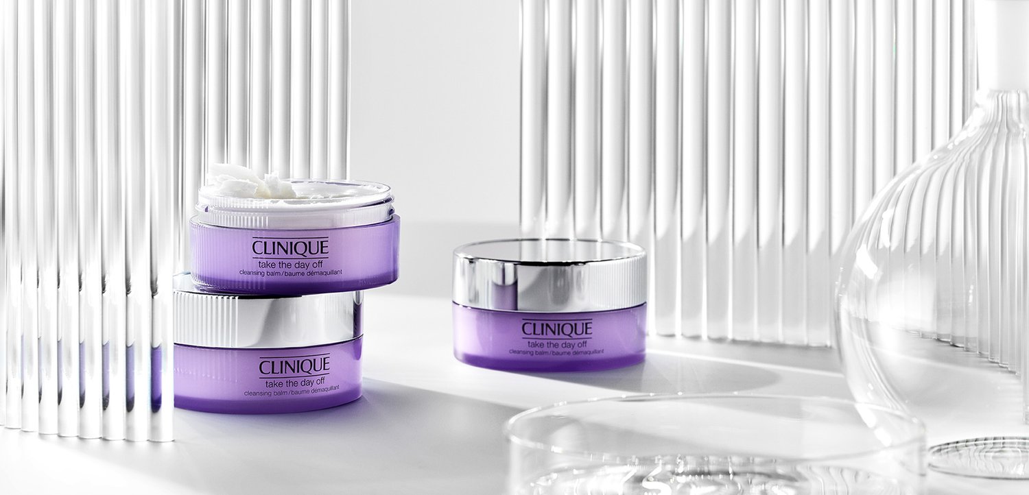CLINIQUE Reinigungsbalsam in einem lila Behälter mit silbernem Deckel, versehen mit geprägtem Text und einer glatten, cremigen Textur, neben einem ähnlichen Glas gestapelt.