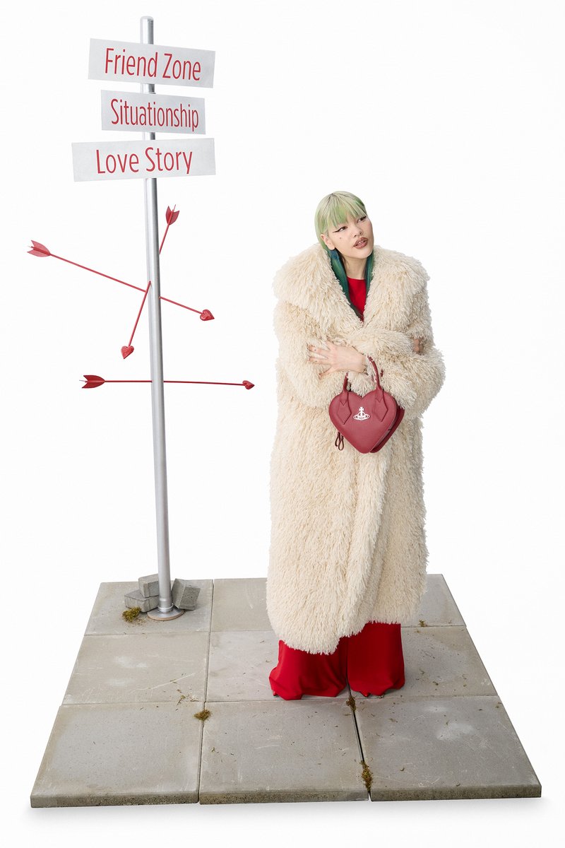 A person with green hair wears a fluffy coat and holds a heart-shaped bag, standing beside a signpost with romantic relationship terms.