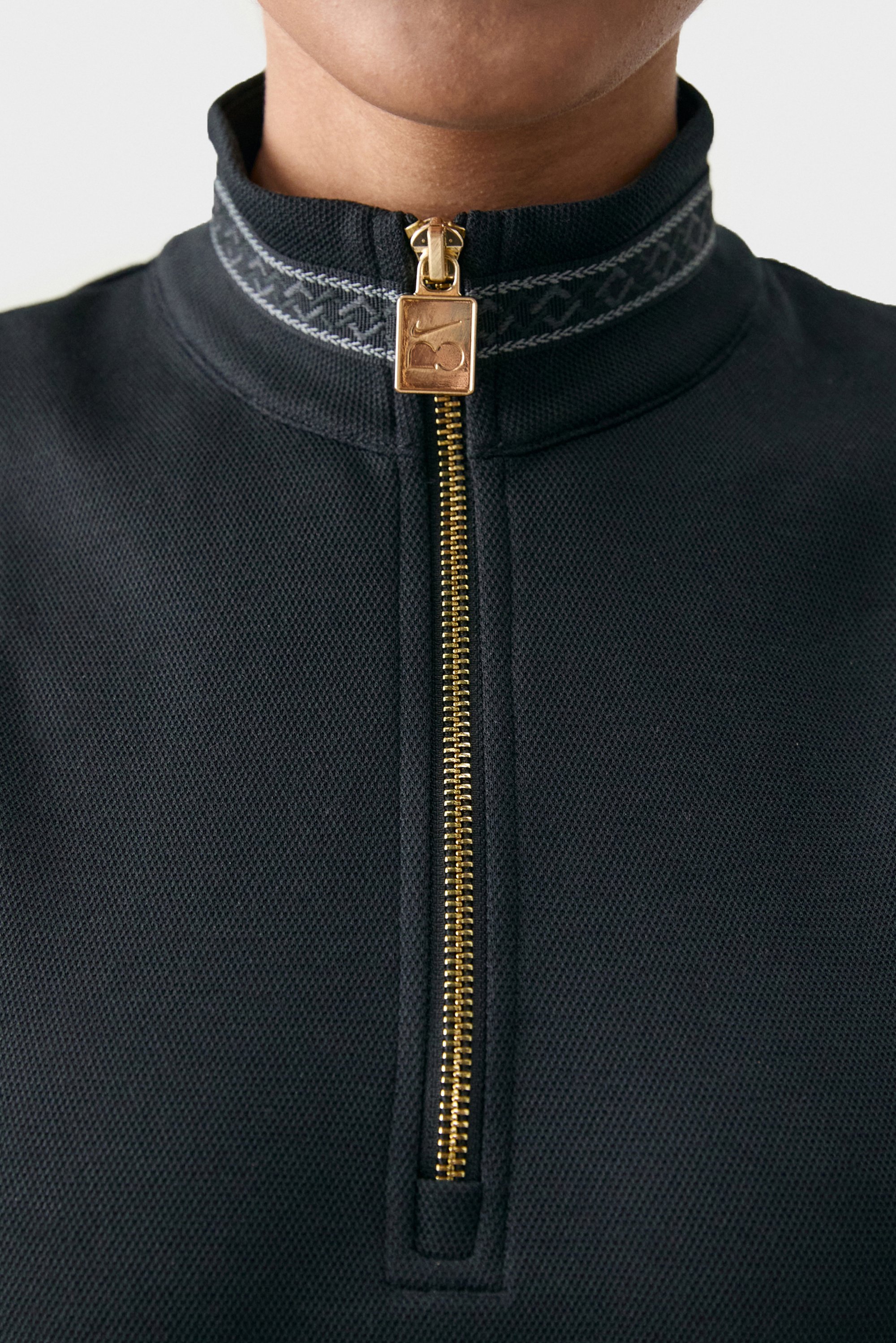 Primer plano de una prenda negra con cremallera, con una cremallera dorada y un detalle de cuello estampado, destacando su textura y características de diseño.