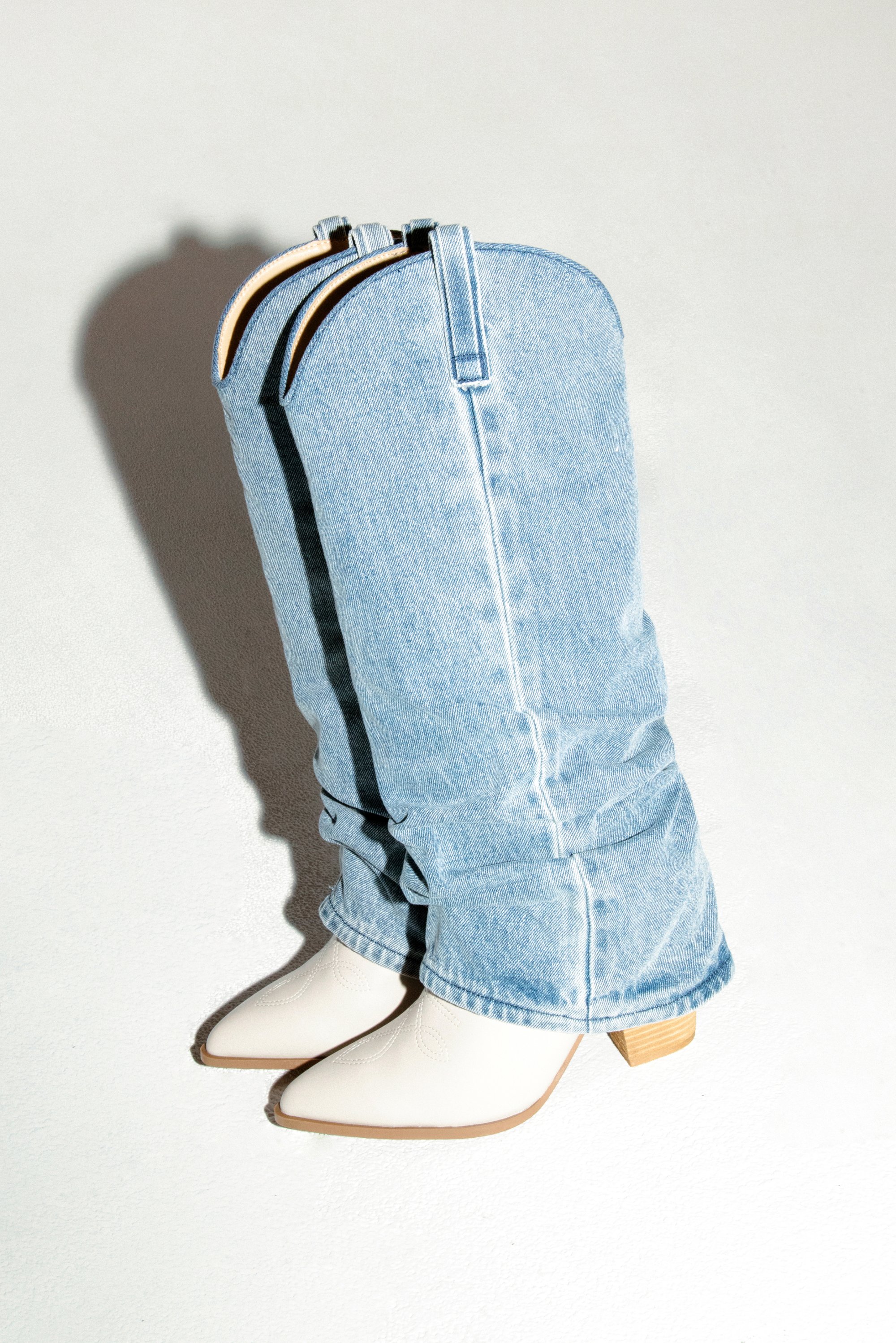 Il tessuto di denim forma una struttura a boucle unica, con stivali bianchi appuntiti che spuntano dal fondo su uno sfondo chiaro.