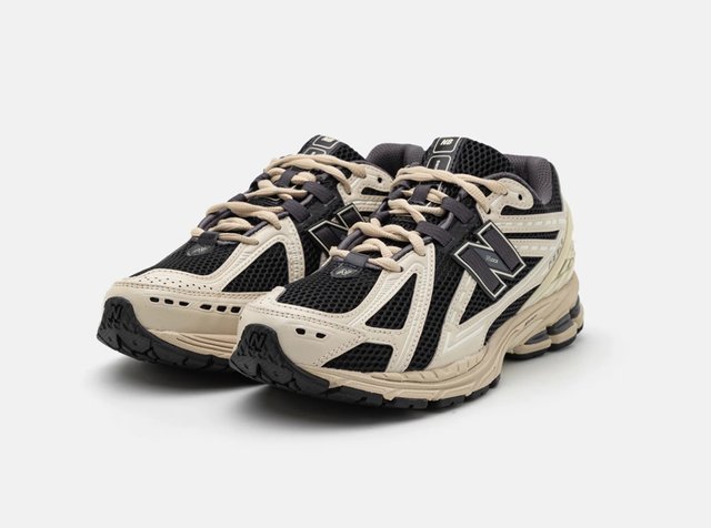 Paire de chaussures de course New Balance noires et beiges avec tissu en mesh et semelles épaisses rembourrées sur fond blanc.