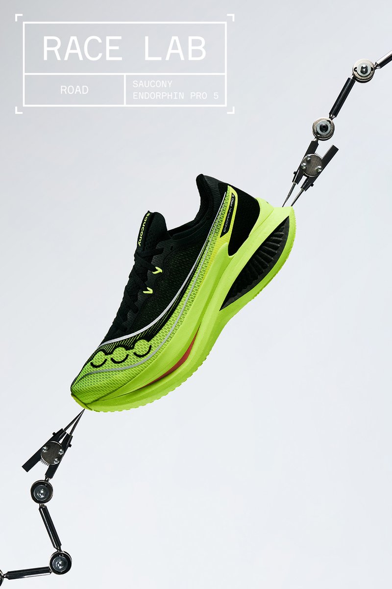 Zwarte en neon groene Saucony Endorphin Pro 5 hardloopschoen opgehangen aan mechanische armen tegen een effen achtergrond.